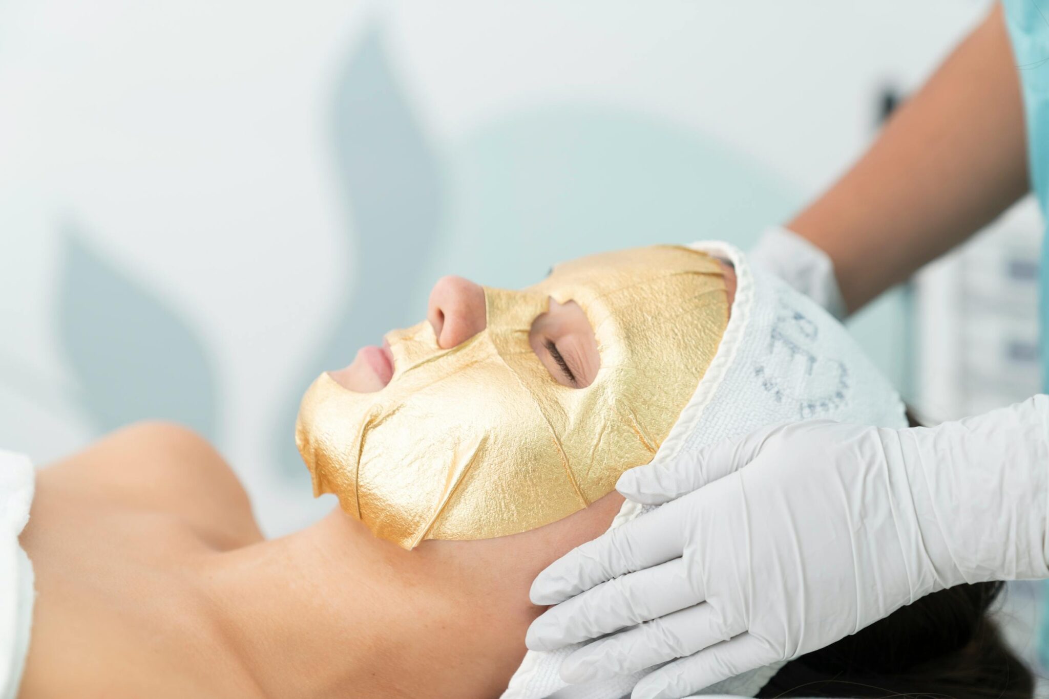 Close-up of a woman receiving a gold facial mask treatment at a spa, promoting relaxation.