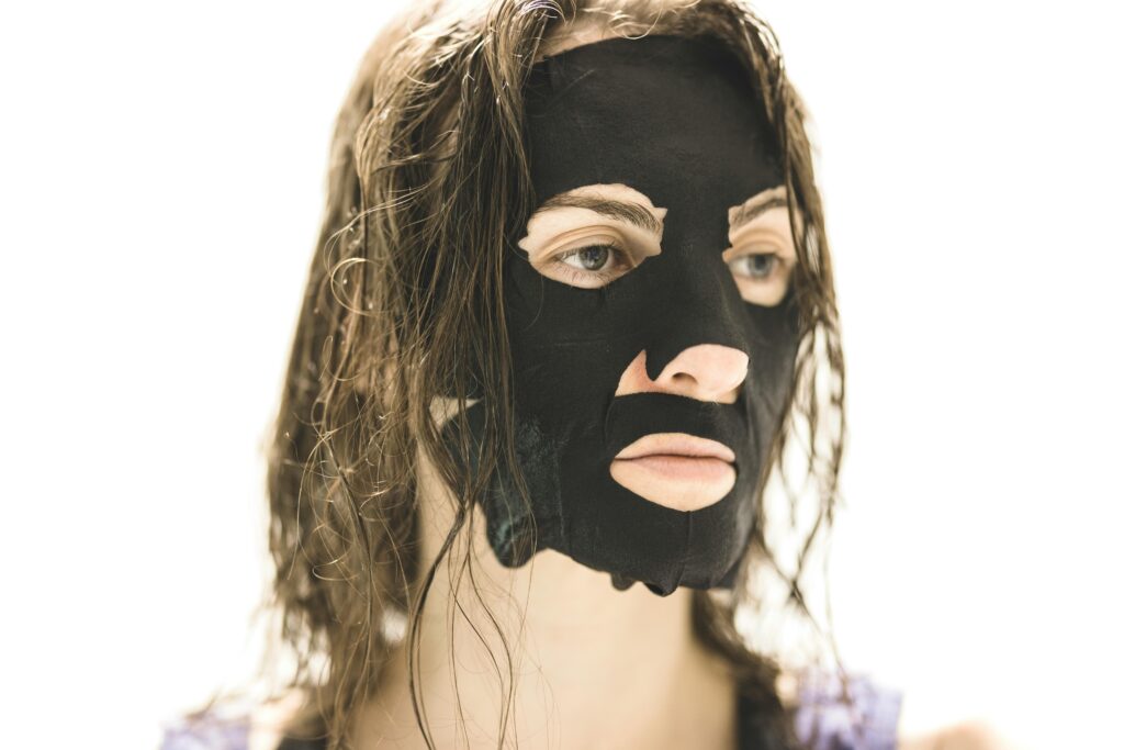 A woman applying a black facial mask for skincare and rejuvenation.