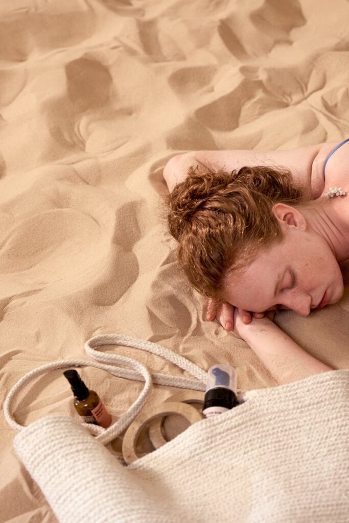 A woman in a swimsuit sleeping peacefully on a sandy beach with seashells on her back.